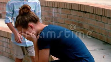 小学生在校园的台阶上安慰她悲伤的朋友